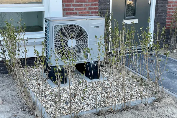 Eine Wärmepumpe steht vor einem Haus auf einem Rasenstück. 